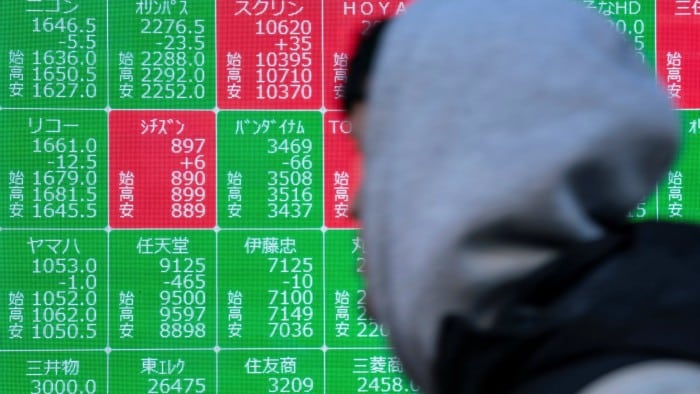 A man walk past an electronic board showing stock prices in Tokyo