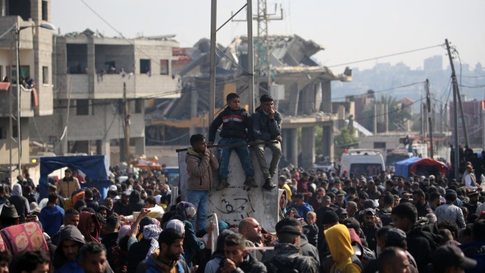 Displaced Palestinians wait along the Salah al-Din road in Nuseirat near the blocked Netzarim corridor, to cross to the northern part of the Gaza Strip on Sunday