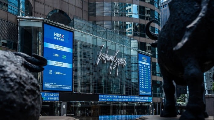 The Exchange Square Complex in Hong Kong features a large digital display showing financial data. Statues of bulls are visible in the foreground.