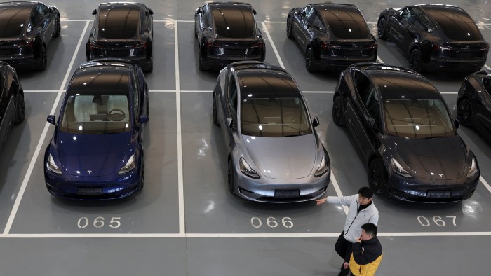 Tesla electric vehicles are parked in a delivery centre in Beijing. Two people walk past the cars