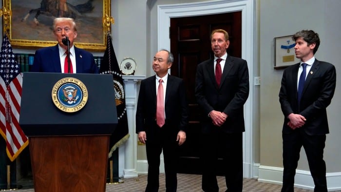 President Donald Trump speaks on a podium while Masayoshi Son, Larry Ellison and Sam Altman listen on the side