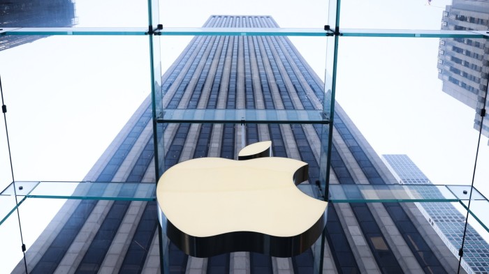 The Apple logo is prominently displayed on a glass structure, with a tall skyscraper in the background in New York City.