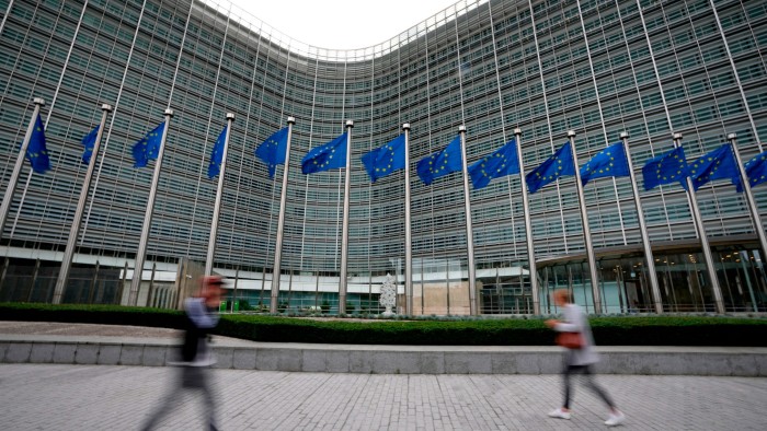 EU flags wave in the wind as pedestrians walk by its headquarters in Brussels