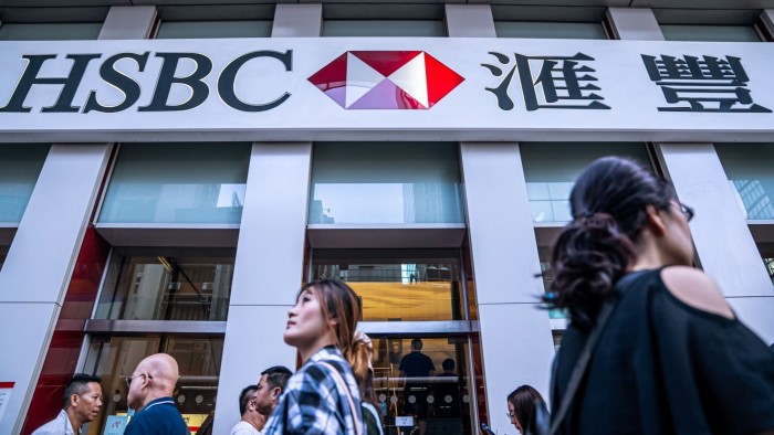 Exterior of an HSBC branch in Hong Kong, with people walking past. The signage displays the HSBC logo and Chinese characters above the entrance.