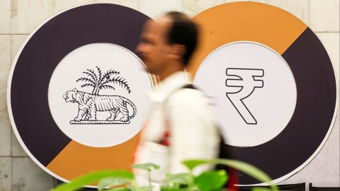 A man walks past logos of the Reserve Bank of India and the rupee