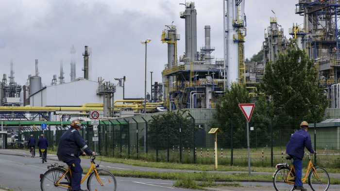 Workers cycle towards an entrance gate to the Ruhr oil refinery operated by BP in Germany