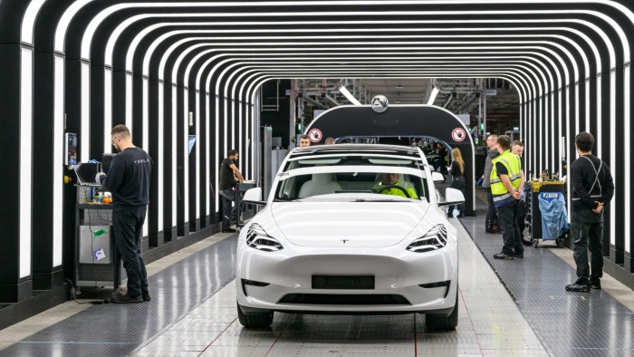 Employees conduct a final inspection of a white Tesla Model Y electric vehicle at the Tesla Gigafactory Berlin-Brandenburg.