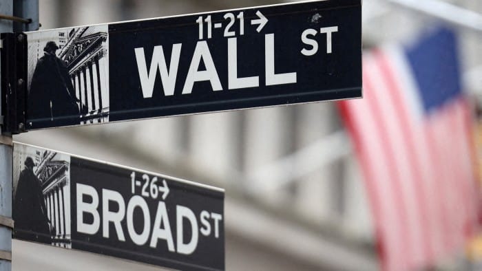 A Wall Street sign hangs in front of a US flag outside the New York Stock Exchange