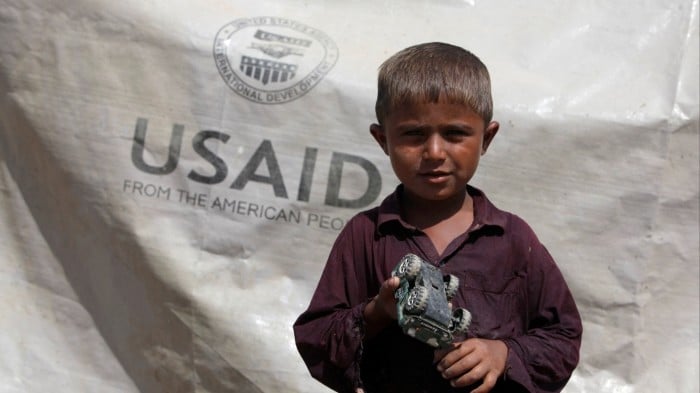 A boy who has been displaced by flooding outside his family tent with the weather sheet donated by USAID,