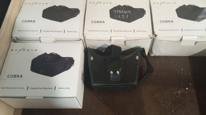 Boxes of Skyzone Cobra goggles are displayed, with one pair of black goggles placed in front of the boxes.