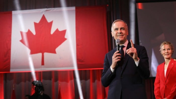 Mark Carney and Diana Carney on stage with the flag of Canada behind them