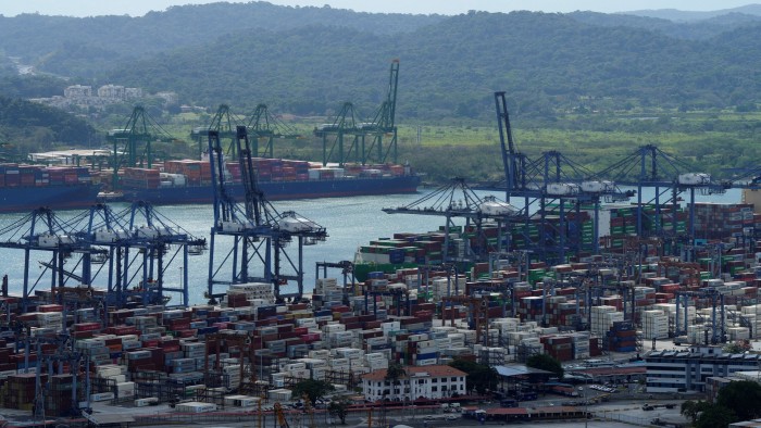 Aerial view of Balboa Port with numerous shipping containers and large cranes and a backdrop of green hills and distant buildings