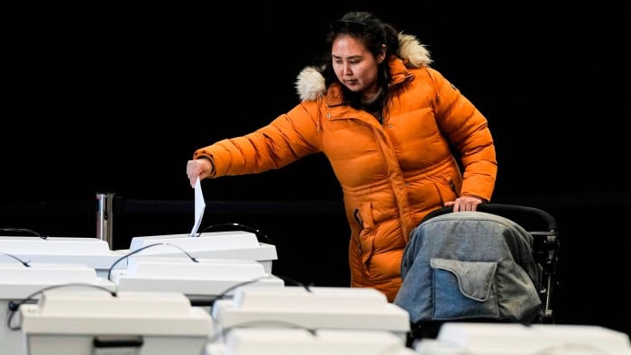 A woman wearing an orange coat casts her vote at a polling station while standing next to a stroller