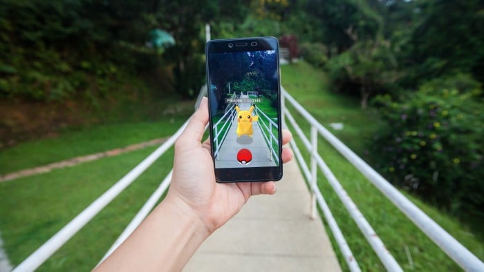 Hand holding a cell phone playing Pokémon Go game in footpath