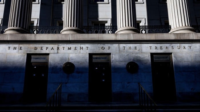 The front facade of the US Treasury building in Washington with tall columns and the inscription &quot;THE DEPARTMENT OF THE TREASURY.&quot; Shadows partially cover the lower portion of the building.