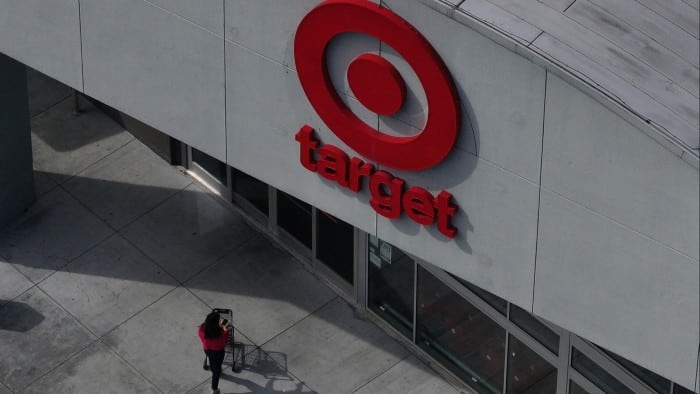 Aerial view of a person entering a Target store, with the large red logo prominently displayed on the building's exterior and the person pushing a shopping trolley towards the entrance