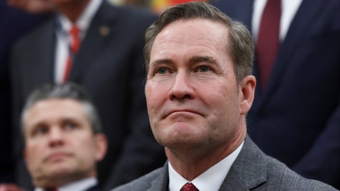 Mike Waltz is seen sitting attentively. In the background is Pete Hegseth