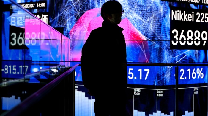 A man stands before a stock market indicator board in Tokyo, Japan