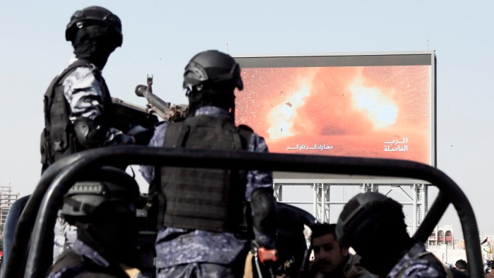 Yemen’s Houthi forces ride a vehicle next to a large screen broadcasting an attack of Yemen’s Houthis targeted a US battleship in the Red Sea