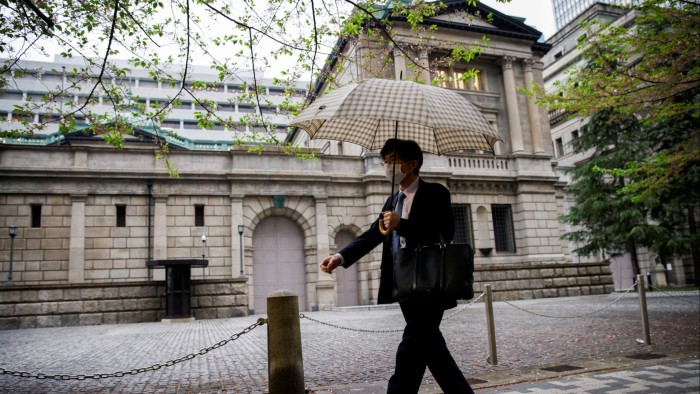 An office employee, wearing a face mask and holding an umbrella, walks past the Bank of Japan building in Tokyo