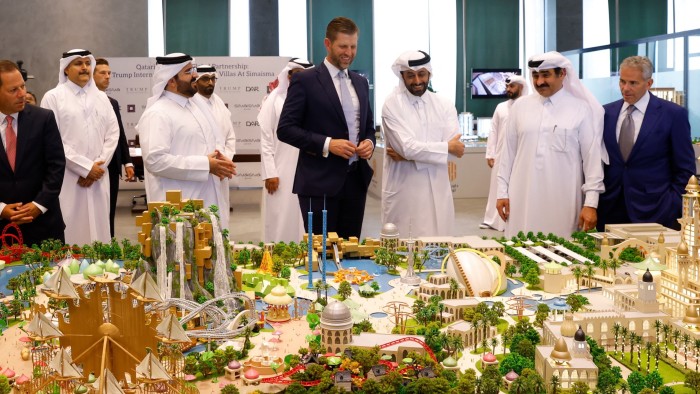 Eric Trump is examining a detailed scale model of a development project alongside several Qatari officials dressed in traditional white garments
