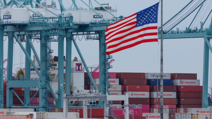 A US flag flutters near shipping containers as a ship is unloaded at the Port of Los Angeles