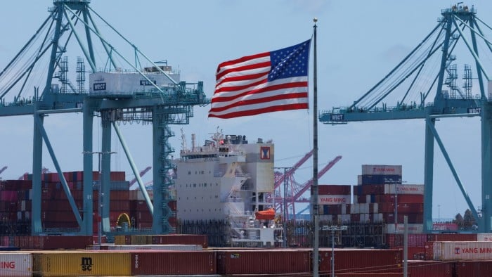 An American flag flies over a ship and containers in Los Angeles port
