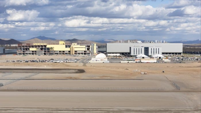 The TSMC fabrication plant in Phoenix, Arizona, with expansive industrial buildings under a cloudy sky, surrounded by desert landscape