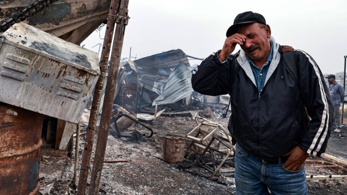 Palestinian farmer Ahmad Khalil reacts as he stands amid the charred remains of his agricultural installation