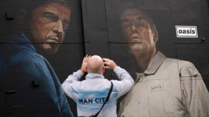 A man takes photographs of an Oasis mural ahead of their concerts in Heaton Park