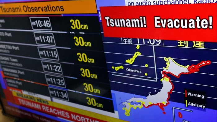 A television screen shows a news report on Japan Weather Agency’s tsunami warning