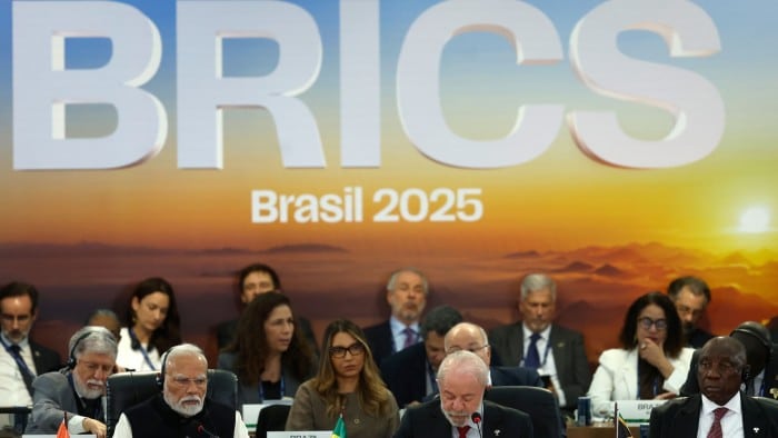 Leaders and delegates at a Brics summit sit at a conference table in front of a large backdrop reading ‘BRICS Brasil 2025’