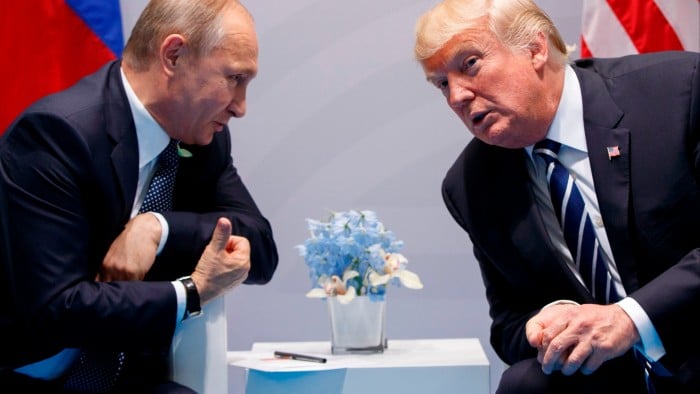 Vladimir Putin and Donald Trump sitting next to each other and leaning towards each other.
