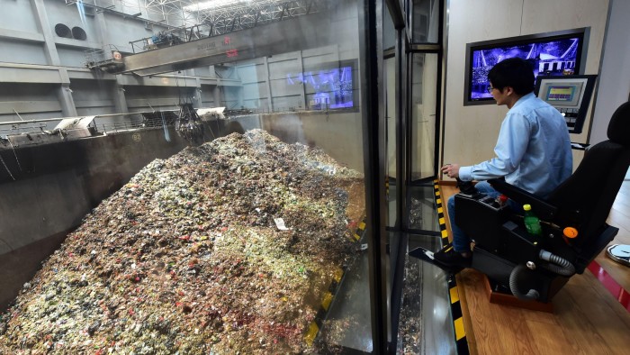 A worker sits at a control station overlooking a large pile of trash at the Solid Waste Incineration Plant in Nanjing, monitoring the incineration process.