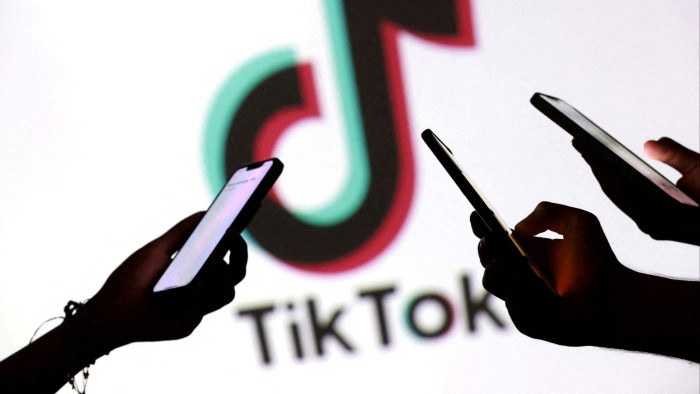 Silhouetted hands holding smartphones in front of a large TikTok logo.