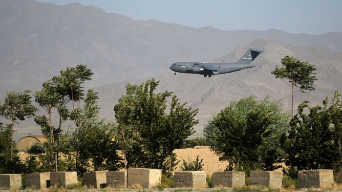 A US Air Force transport plane descends to land at Bagram Air Base, with trees and mountains in the background.